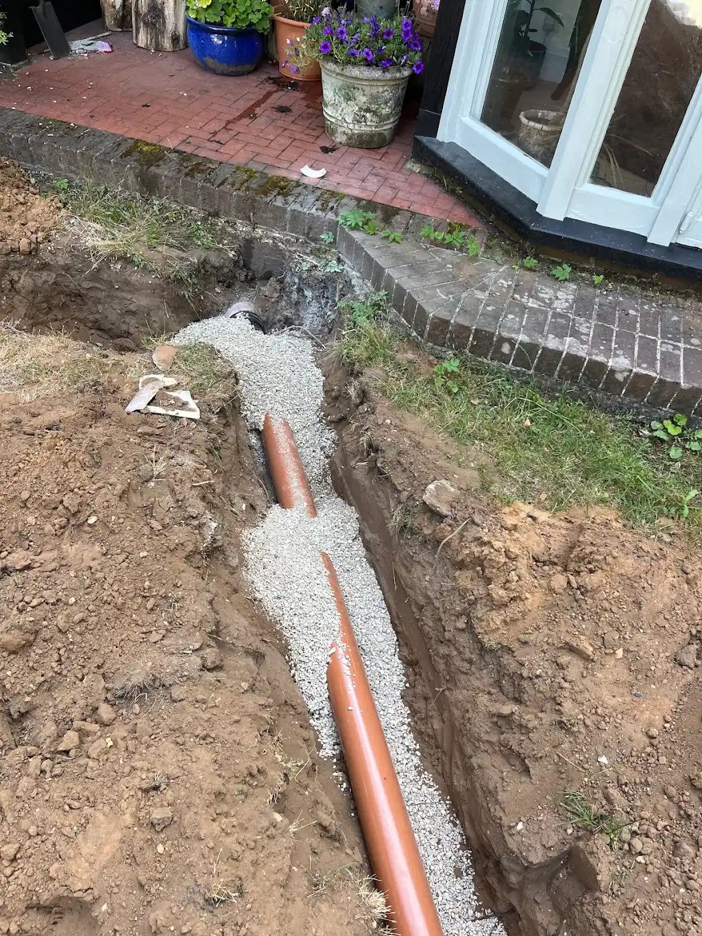 Close-up of drainage pipe bedded in pea shingle next to the patio
